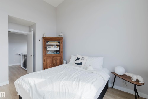 Bedroom with light-colored walls and flooring, featuring a bed with white bedding, a wooden cabinet with glass doors, and a side table with a white spherical lamp - 1129 Keswick Drive, Edmonton, AB - Indoor Photo Showing Bedroom