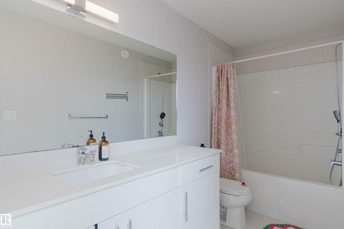 Bathroom featuring a spacious vanity with a white countertop, a large wall-mounted mirror, and a bathtub with a shower - 1129 Keswick Drive, Edmonton, AB - Indoor Photo Showing Bathroom