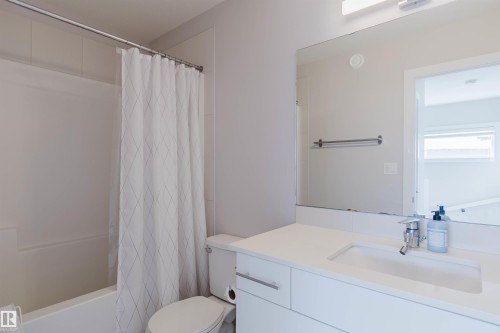 The bathroom includes a modern vanity with a white countertop and an integrated sink, a toilet, and a bathtub with a shower curtain - 1129 Keswick Drive, Edmonton, AB - Indoor Photo Showing Bathroom