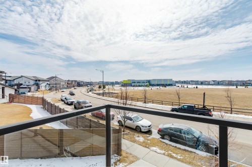 The property features a balcony with a glass railing and offers views of a residential street, a large field, and distant buildings - 1129 Keswick Drive, Edmonton, AB - Outdoor With Balcony With View