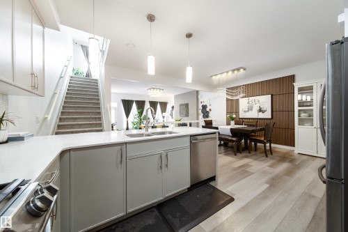The property features an open-concept living area with light wood flooring, a modern kitchen island with a sink and stainless steel dishwasher, and a staircase with carpeted treads - 22931 96 Avenue, Edmonton, AB - Indoor Photo Showing Kitchen With Double Sink With Upgraded Kitchen