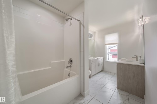 Bathroom featuring a white bathtub with a shower, a vanity with a sink and faucet, a window with a blind, and tiled flooring - 22931 96 Avenue, Edmonton, AB - Indoor Photo Showing Bathroom