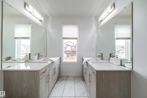 The bathroom features dual vanities with light wood cabinetry, white countertops, and expansive wall-mounted mirrors - 22931 96 Avenue, Edmonton, AB - Indoor Photo Showing Bathroom
