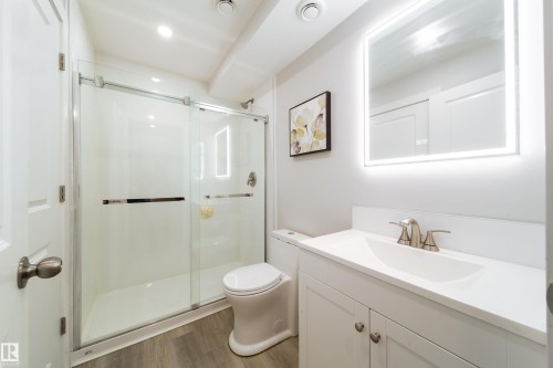 The bathroom features a glass-enclosed shower, a vanity with a white countertop and sink, and a backlit mirror - 22931 96 Avenue, Edmonton, AB - Indoor Photo Showing Bathroom