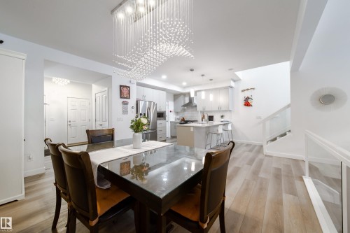 This open-concept main level features light-toned flooring, a contemporary kitchen with stainless steel appliances, and a modern dining area with a distinctive chandelier - 22931 96 Avenue, Edmonton, AB - Indoor Photo Showing Dining Room