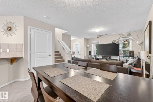 The open concept living area features a dining space with a dark wood table, carpeted floors, and a stairway with white railings - 219 60 Street, Edmonton, AB - Indoor