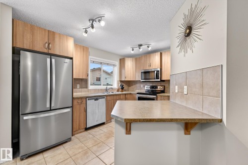 The kitchen features stainless steel appliances, including a refrigerator, dishwasher, and microwave - 219 60 Street, Edmonton, AB - Indoor Photo Showing Kitchen With Double Sink