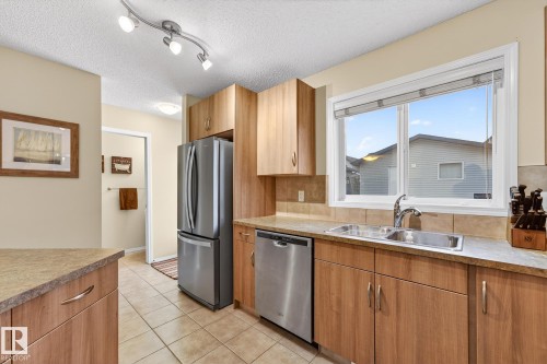 The kitchen features light wood cabinetry, a double basin stainless steel sink, and a stainless steel dishwasher - 219 60 Street, Edmonton, AB - Indoor Photo Showing Kitchen With Double Sink