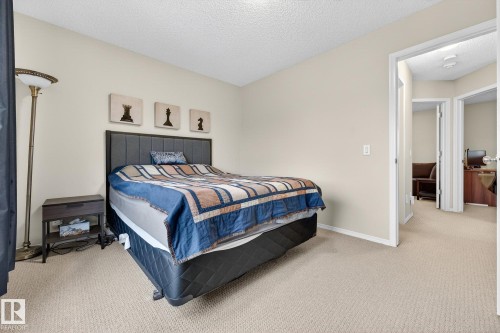 The property features a bedroom with neutral-toned walls and carpeting, a bed with a dark headboard, and a floor lamp with a brass finish - 219 60 Street, Edmonton, AB - Indoor Photo Showing Bedroom