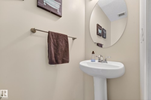 Pedestal sink with a chrome faucet, illuminated by overhead lighting, and an oval mirror - 219 60 Street, Edmonton, AB - Indoor Photo Showing Bathroom