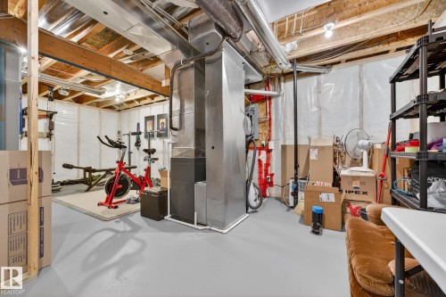 The property features a utility area with exposed ceiling joists and ductwork, painted concrete flooring, and a portion of the wall covered with plastic sheeting - 219 60 Street, Edmonton, AB - Indoor Photo Showing Basement