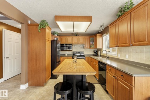 The kitchen features wood cabinetry, dark countertops, and a central island with a wood surface - 12815 156 Avenue, Edmonton, AB - Indoor Photo Showing Kitchen