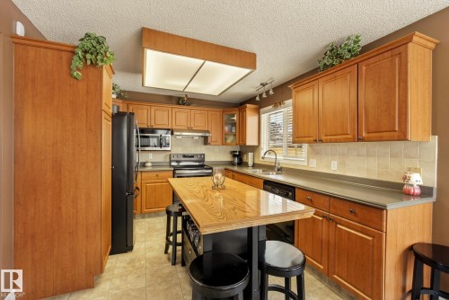 The kitchen features wood cabinetry, a central island with an extended countertop, and a tiled backsplash - 12815 156 Avenue, Edmonton, AB - Indoor Photo Showing Kitchen With Double Sink