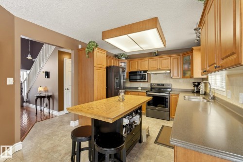 The kitchen features wood cabinetry, a central island with a wood countertop, and a stainless steel sink with a window above - 12815 156 Avenue, Edmonton, AB - Indoor Photo Showing Kitchen With Double Sink