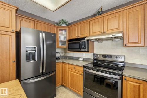 The kitchen features wooden cabinetry, a stainless steel refrigerator, and a built-in microwave - 12815 156 Avenue, Edmonton, AB - Indoor Photo Showing Kitchen
