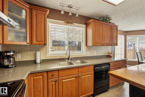 The kitchen features wood cabinetry, a double basin sink, and a black dishwasher - 12815 156 Avenue, Edmonton, AB - Indoor Photo Showing Kitchen With Double Sink