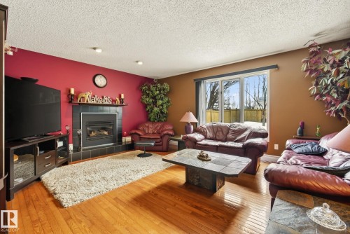 The living room features hardwood flooring, a fireplace with a dark tile surround, and large windows providing views of the outdoors - 12815 156 Avenue, Edmonton, AB - Indoor Photo Showing Living Room With Fireplace
