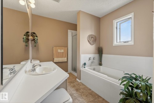 Bathroom featuring a vanity with an integrated sink and chrome faucet, a built-in bathtub with a white tiled surround, and a clear glass shower enclosure - 12815 156 Avenue, Edmonton, AB - Indoor