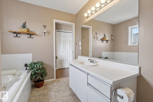 Bathroom featuring a vanity with a white countertop and a built-in sink, a large mirror, and a bathtub - 12815 156 Avenue, Edmonton, AB - Indoor Photo Showing Bathroom