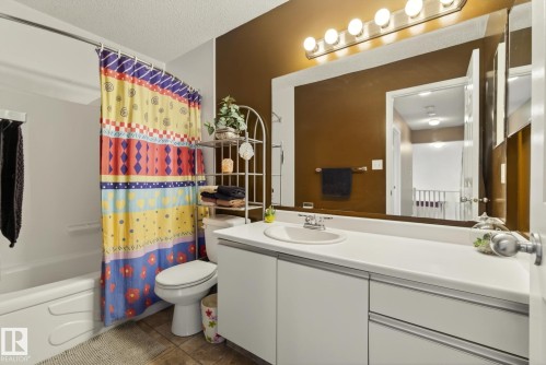 This bathroom features a spacious vanity with an integrated sink, a large mirror with overhead lighting, and a bathtub with a shower - 12815 156 Avenue, Edmonton, AB - Indoor Photo Showing Bathroom