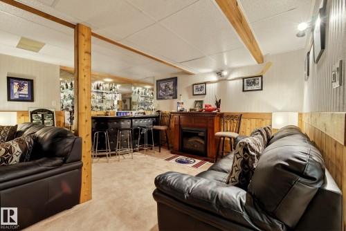 This versatile space features carpeting, a wooden accent wall, and a built-in bar with seating - 12815 156 Avenue, Edmonton, AB - Indoor With Fireplace