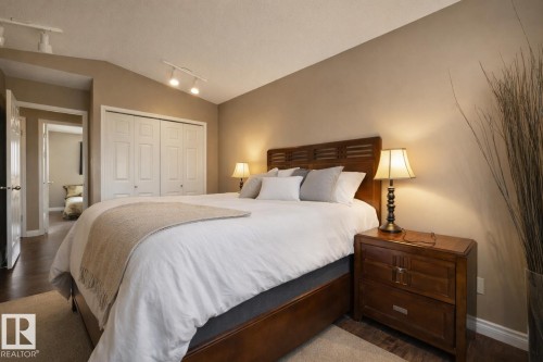 This inviting bedroom features warm beige walls, rich hardwood flooring, and a vaulted ceiling with track lighting - 12815 156 Avenue, Edmonton, AB - Indoor Photo Showing Bedroom