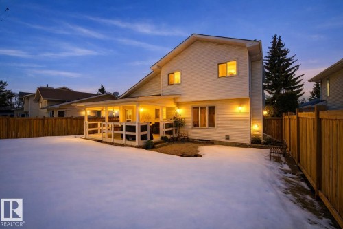 The property features a fenced yard with a snow-covered lawn and a covered patio area, illuminated by several exterior lights - 12815 156 Avenue, Edmonton, AB - Outdoor With Deck Patio Veranda