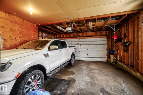 This property features a garage with a paneled wood wall, an overhead garage door, and exposed ceiling joists - 12815 156 Avenue, Edmonton, AB - Indoor Photo Showing Garage