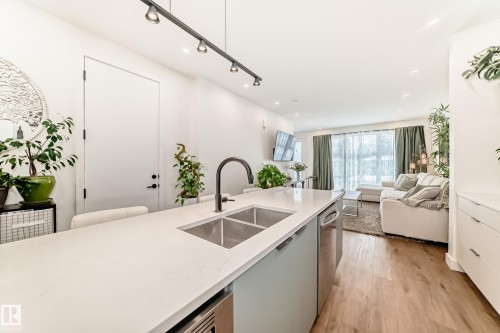 The kitchen features a spacious island with a double stainless steel sink and a contemporary faucet - 10936 117 Street, Edmonton, AB - Indoor Photo Showing Kitchen With Double Sink