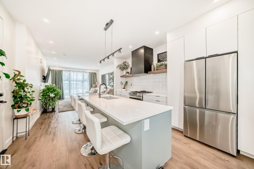 The kitchen features a spacious island with a light-colored countertop and a light-toned base, complemented by stainless steel appliances - 10936 117 Street, Edmonton, AB - Indoor Photo Showing Kitchen With Upgraded Kitchen