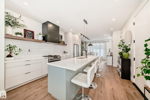 The kitchen features a large island with a light countertop, a stainless steel range, and a sleek black range hood - 10936 117 Street, Edmonton, AB - Indoor Photo Showing Kitchen With Upgraded Kitchen