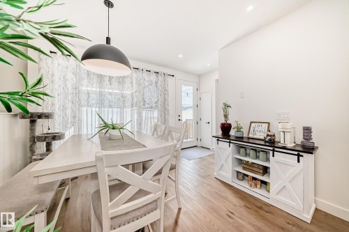 Dining area featuring light-toned flooring, a modern pendant light fixture, and a white barn door style console cabinet - 10936 117 Street, Edmonton, AB - Indoor Photo Showing Dining Room