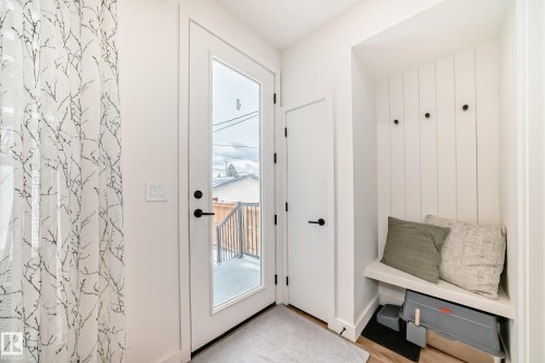 Entryway featuring a white door with a glass panel, a built-in bench with coat hooks, and light hardwood flooring - 10936 117 Street, Edmonton, AB - Indoor Photo Showing Other Room
