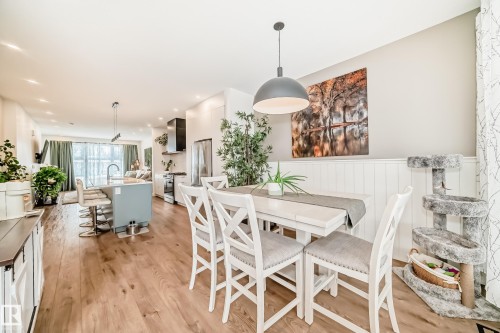This open-concept living area features hardwood floors, a light-colored dining table with white chairs, and a kitchen island with seating - 10936 117 Street, Edmonton, AB - Indoor Photo Showing Dining Room