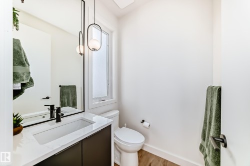 This powder room features a vanity with a white countertop and dark cabinetry, a rectangular sink with a matte black faucet, and a large wall mirror - 10936 117 Street, Edmonton, AB - Indoor Photo Showing Bathroom