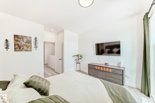 This bedroom features light-colored walls and flooring, with a window dressed in green curtains providing natural light - 10936 117 Street, Edmonton, AB - Indoor Photo Showing Bedroom