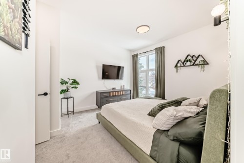 This room features light-colored walls, carpeted flooring, and a large window providing natural light - 10936 117 Street, Edmonton, AB - Indoor Photo Showing Bedroom