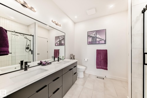 The bathroom features a dual vanity with a white countertop and dark cabinetry, a spacious mirror, and a shower with a clear glass enclosure - 10936 117 Street, Edmonton, AB - Indoor Photo Showing Bathroom