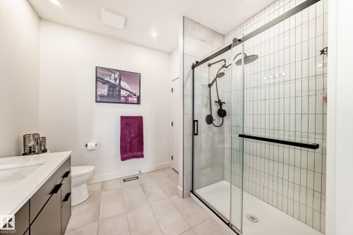 Bathroom featuring a glass-enclosed shower with black fixtures, a floating vanity with a white countertop, and light-colored floor tiles - 10936 117 Street, Edmonton, AB - Indoor Photo Showing Bathroom