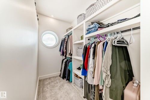 Walk-in closet featuring built-in shelving, hanging rods, carpeted flooring, and a circular window - 10936 117 Street, Edmonton, AB - Indoor With Storage