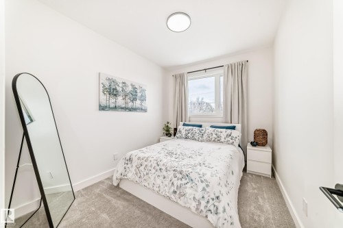This bright space features a window with light-colored curtains, neutral-toned carpeting, and a ceiling-mounted light fixture - 10936 117 Street, Edmonton, AB - Indoor Photo Showing Bedroom