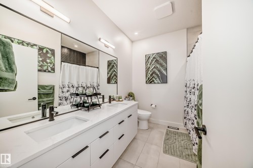 The bathroom features a long vanity with two integrated sinks and ample storage, a large mirror, and a toilet - 10936 117 Street, Edmonton, AB - Indoor Photo Showing Bathroom