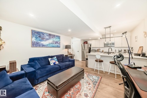 This open-concept living area features light wood flooring, a kitchen island with seating, a stainless steel refrigerator, and pendant lighting - 10936 117 Street, Edmonton, AB - Indoor Photo Showing Living Room