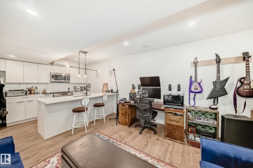 Open-concept living area featuring light wood-style flooring, a kitchen with white cabinetry and stainless steel appliances, and a kitchen island with seating - 10936 117 Street, Edmonton, AB - Indoor Photo Showing Kitchen