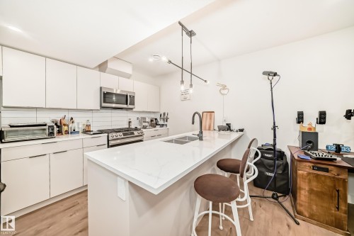 The kitchen features white cabinetry, stainless steel appliances, a white subway tile backsplash, and a large island with a double sink and a contemporary light fixture - 10936 117 Street, Edmonton, AB - Indoor Photo Showing Kitchen With Double Sink With Upgraded Kitchen
