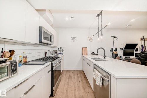 Kitchen featuring white cabinetry, stainless steel appliances, a white subway tile backsplash, and light wood flooring - 10936 117 Street, Edmonton, AB - Indoor Photo Showing Kitchen With Double Sink With Upgraded Kitchen