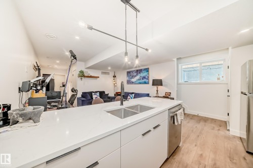 The property features an open concept kitchen and living area, with a white countertop island, double sink, and a modern light fixture - 10936 117 Street, Edmonton, AB - Indoor Photo Showing Kitchen With Double Sink