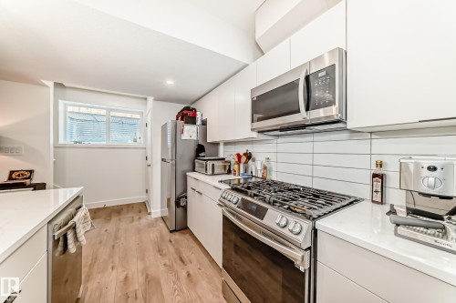 The kitchen features stainless steel appliances, including a gas range and microwave, white cabinetry, white countertops, and a white subway tile backsplash - 10936 117 Street, Edmonton, AB - Indoor Photo Showing Kitchen