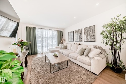 The living room features hardwood flooring, recessed lighting, and large windows with sheer and opaque curtains - 10936 117 Street, Edmonton, AB - Indoor Photo Showing Living Room