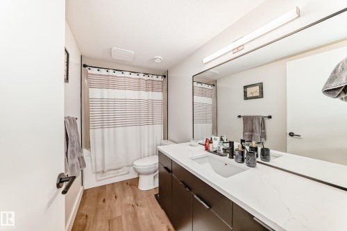 Bathroom featuring wood-style flooring, a large vanity with an integrated sink and light countertop, and a shower with a striped curtain - 10936 117 Street, Edmonton, AB - Indoor Photo Showing Bathroom